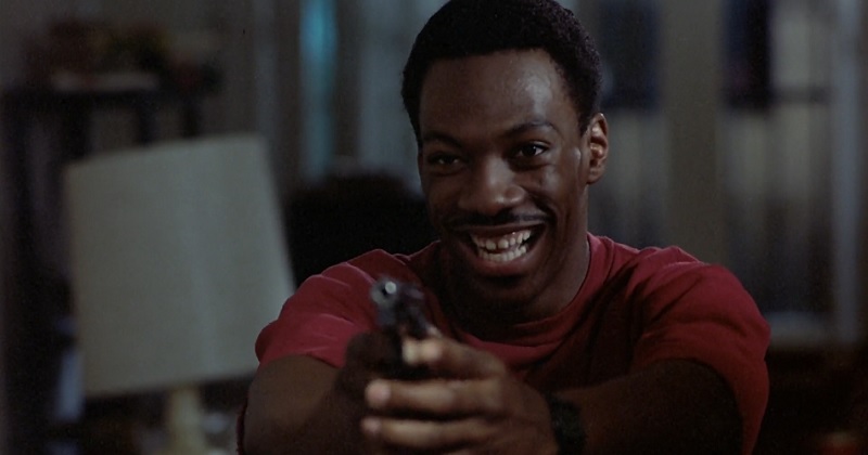 Eddie Murphy plays Axel Foley holding a gun and laughing