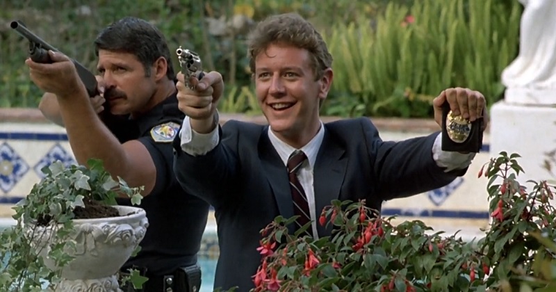Billy Rosewood holding a gun and badge while smiling