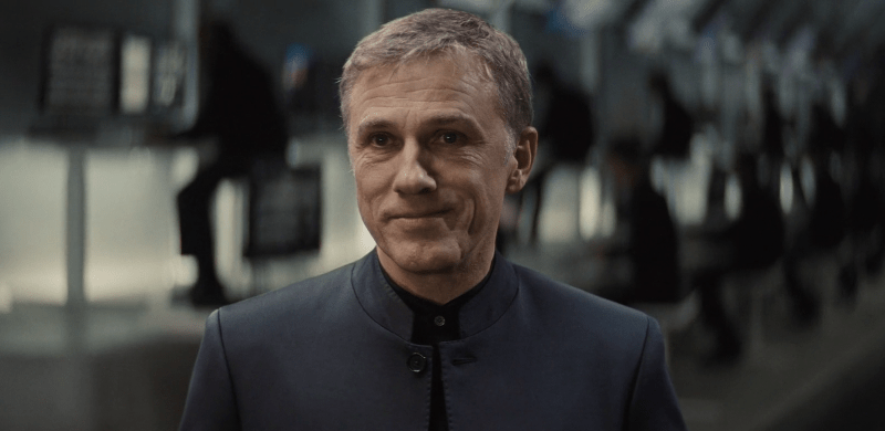 Christoph Waltz gently smiling with five people behind him
