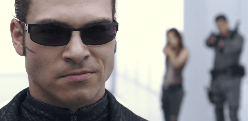 Albert Wesker smiling with glasses on with two people behind him