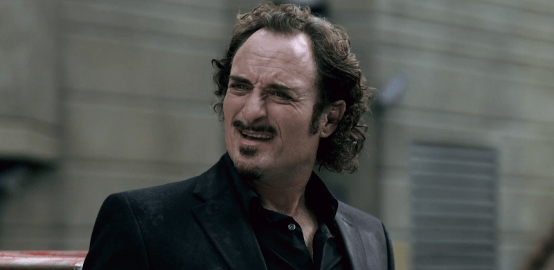 Kim Coates making a snarky face while smiling in a black suit
