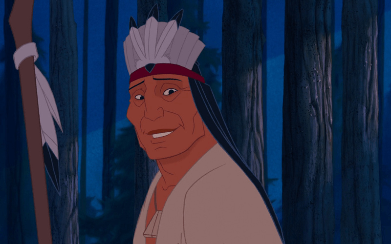 Chief Powhatan smiling with a native american headdress in the forest at night.