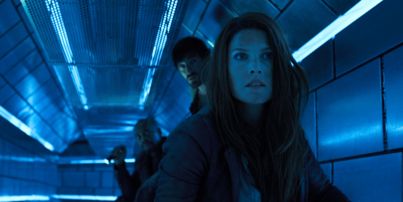 Claire Redfield in a blue tunnel with two men behind her.