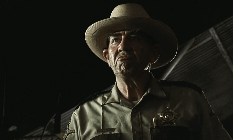 Hoyt wearing a hat and a sheriff uniform while looking disgusted.