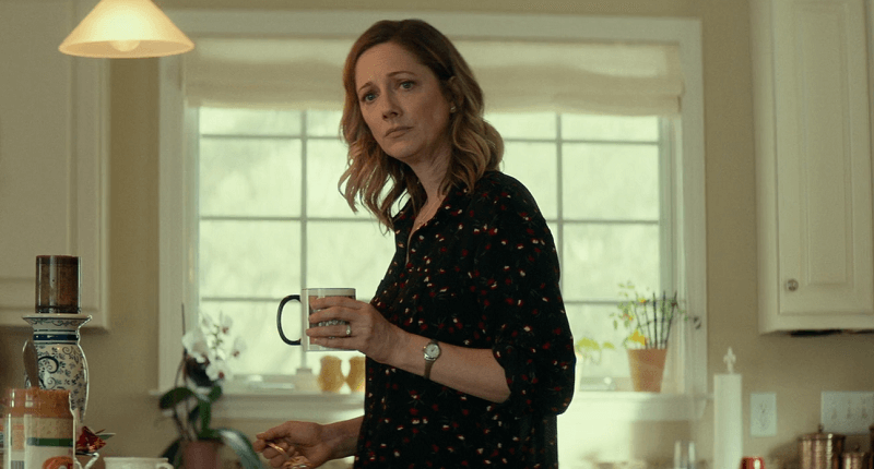 Judy Greer holding a cup in a kitchen looking worried.