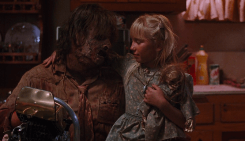 Little blonde girl sitting on the lap of Leatherface.
