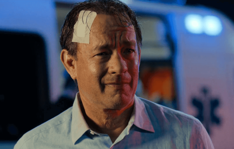 Tom Hanks as Robert Langdon smiling with a large band aid on his head.