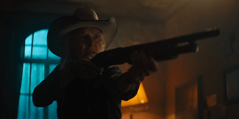 Sally Hardesty with a cowboy hat and a shotgun in a dimly lit room.