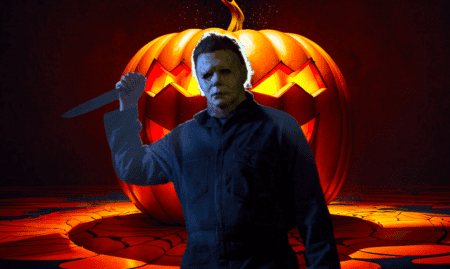 Michael Myers with a kitchen knife in front of a huge orange pumpkin.