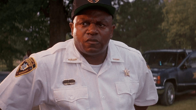 Ozzie Walls in a white cop uniform with a cap and a car behind him.