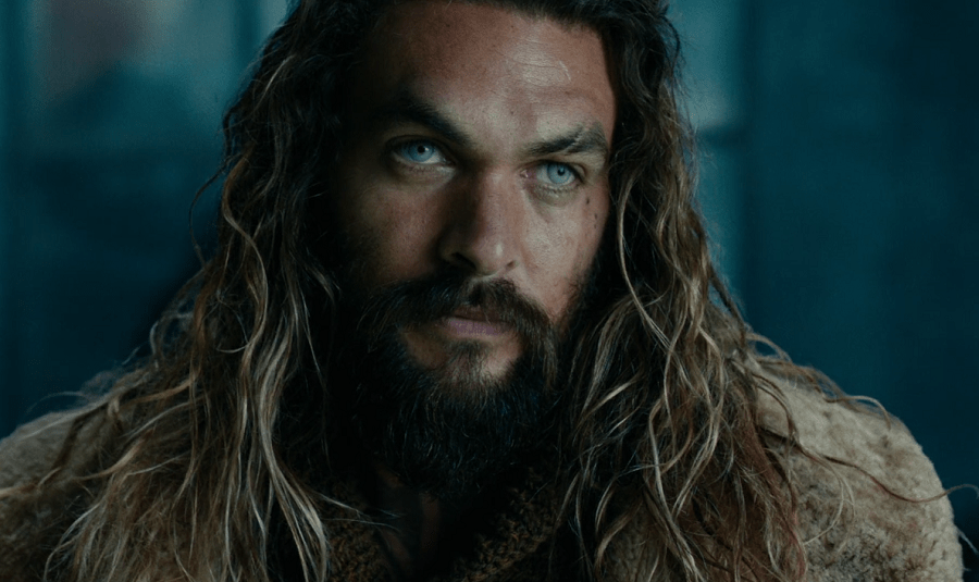 Jason Momoa as Aquaman with blue lenses and long hair in the darkness.