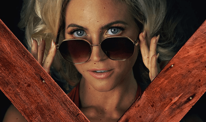 Brittany snow pulling down her sunglasses and looking through two wooden planks.