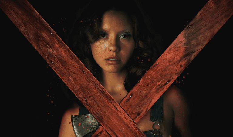Mia Goth as Maxine holding an axe in the dark with two wooden planks forming a cross.