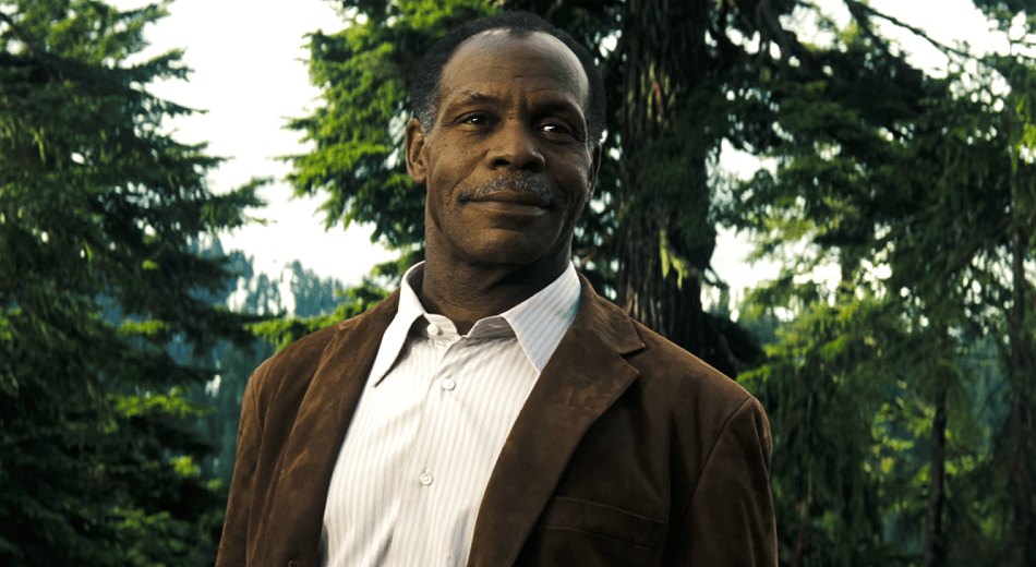 Danny Glover standing tall in a forest with a warm smile.