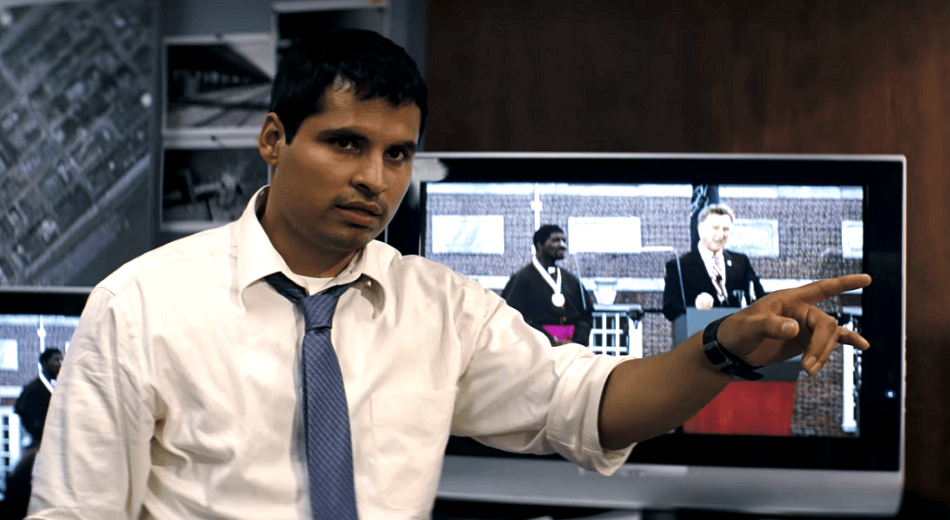 Michael Peña pointing with a TV behiund him while wearing a white shirt.