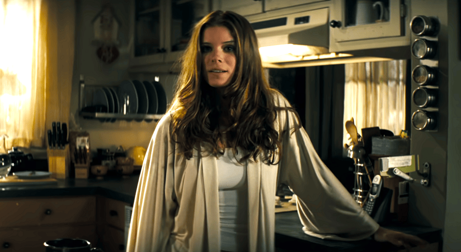 Kate Mara in a beige morning robe in the kitchen looking puzzled.